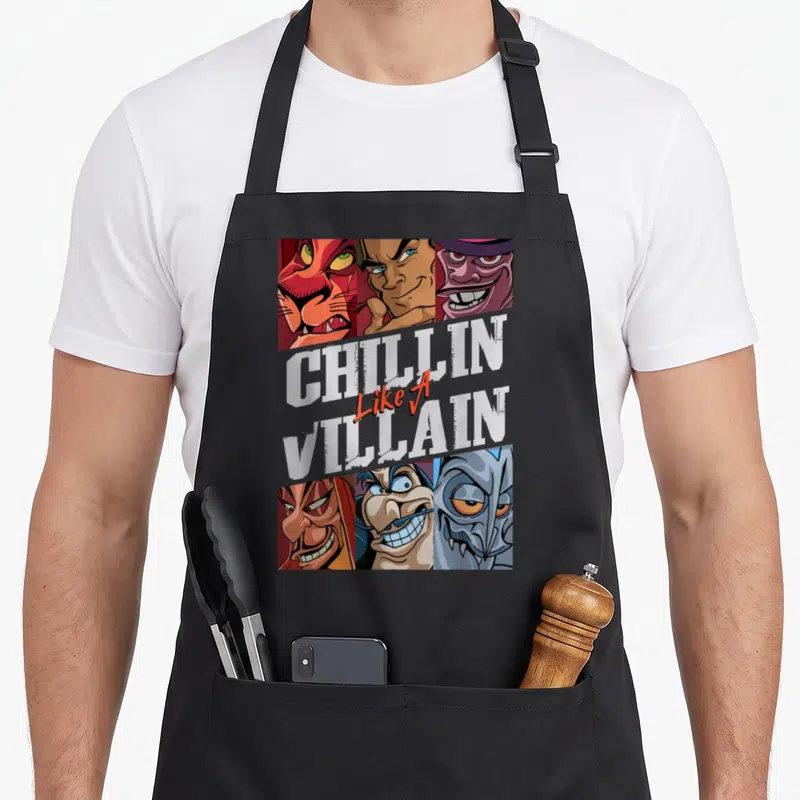 Chillin novelty apron - Six cartoon villain faces surrounding stacked white and red text reading CHILLIN Like A VILLAIN — shown on a black cotton canvas apron against a white background