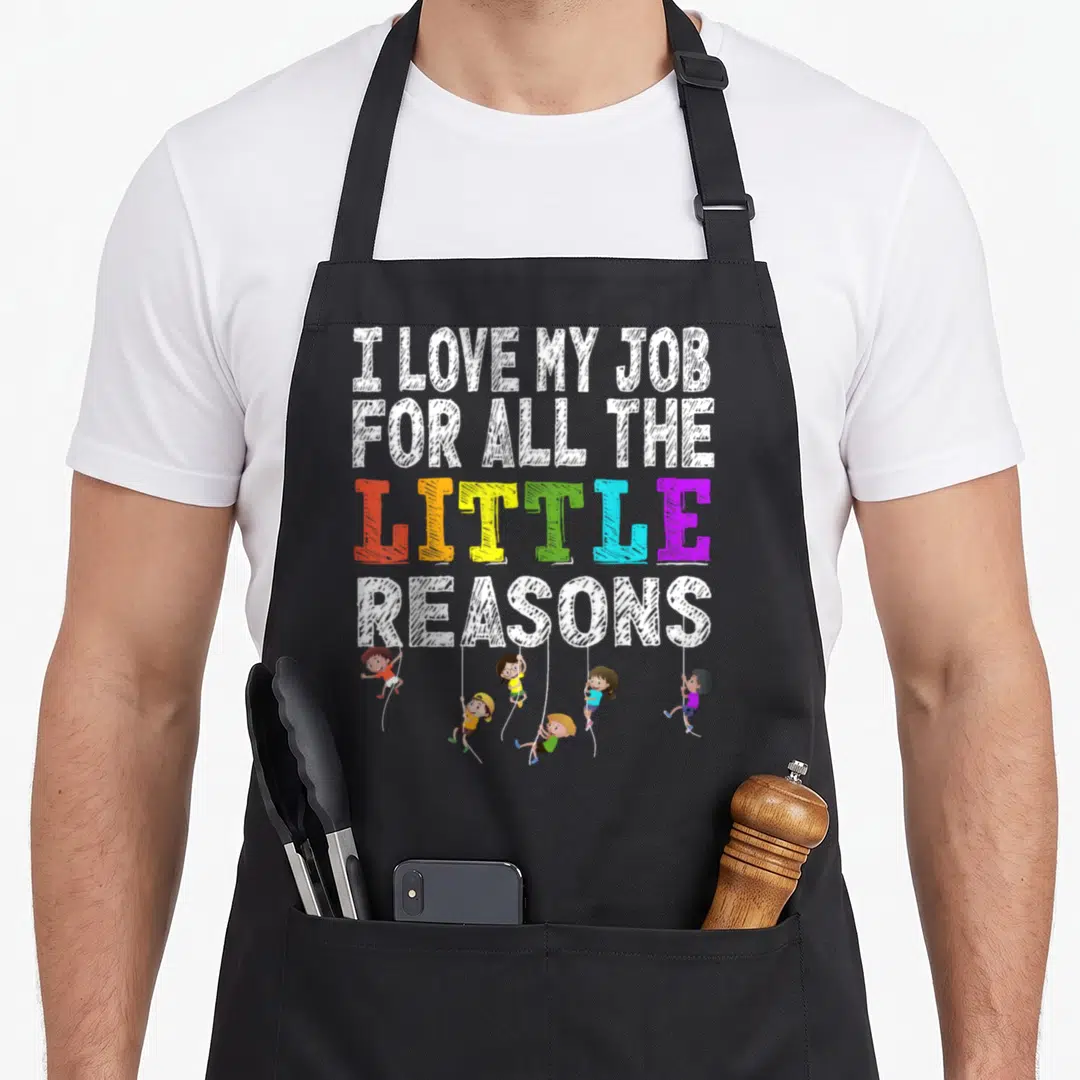 Funny reason teacher apron - Six cartoon children hanging from ropes attached to multicolored and white text reading I — shown on a black cotton canvas apron against a white background