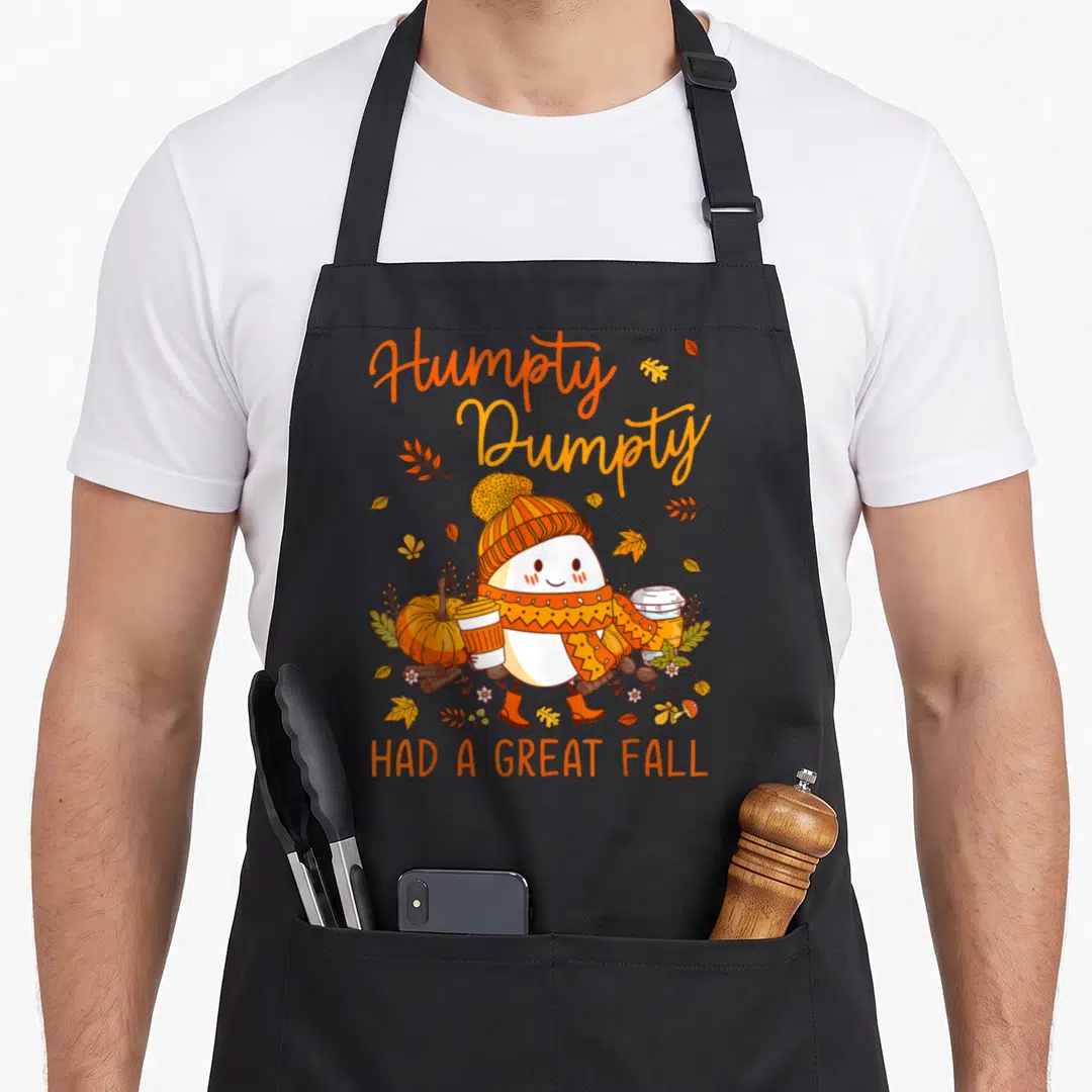 Yall autumn cute fall aprons - Cartoon egg character with scarf and coffee cups surrounded by autumn leaves and pumpkins — shown on a black cotton canvas apron against a white background