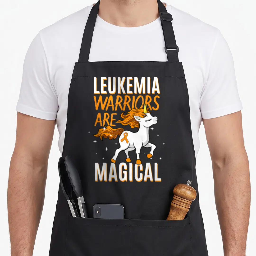 Warrior leukemia awareness apron - White unicorn with orange mane and ribbon surrounded by stars and text — shown on a black cotton canvas apron against a white background