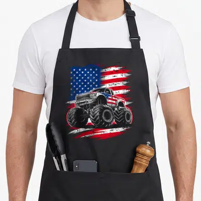 Flag truck aprons - Realistic monster truck with oversized tires in front of a distressed red white and blue flag — shown on a black cotton canvas apron against a white background