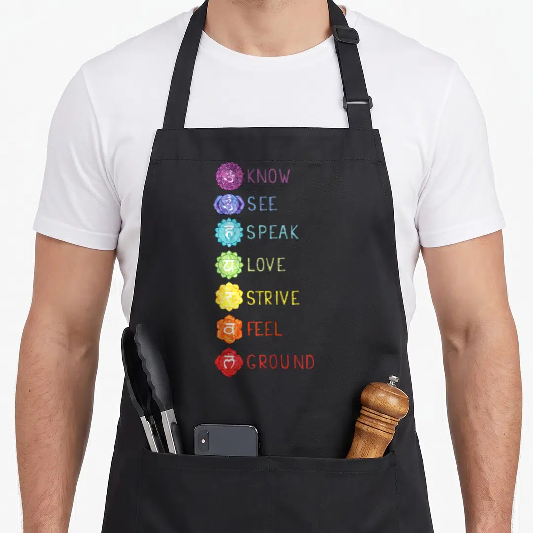 Seven hippie apron - Seven chakras with lotus symbols and words KNOW, SEE, SPEAK, LOVE, STRIVE, FEEL, GROUND in purple — shown on a black cotton canvas apron against a white background