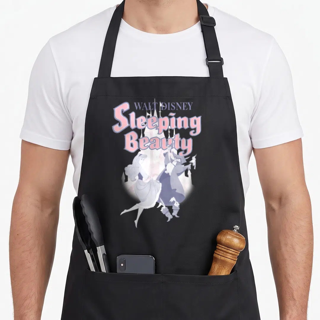 Dancing beauty apron - Sleeping Beauty title text above Aurora and Maleficent with castle in pink and purple cartoon — shown on a black cotton canvas apron against a white background