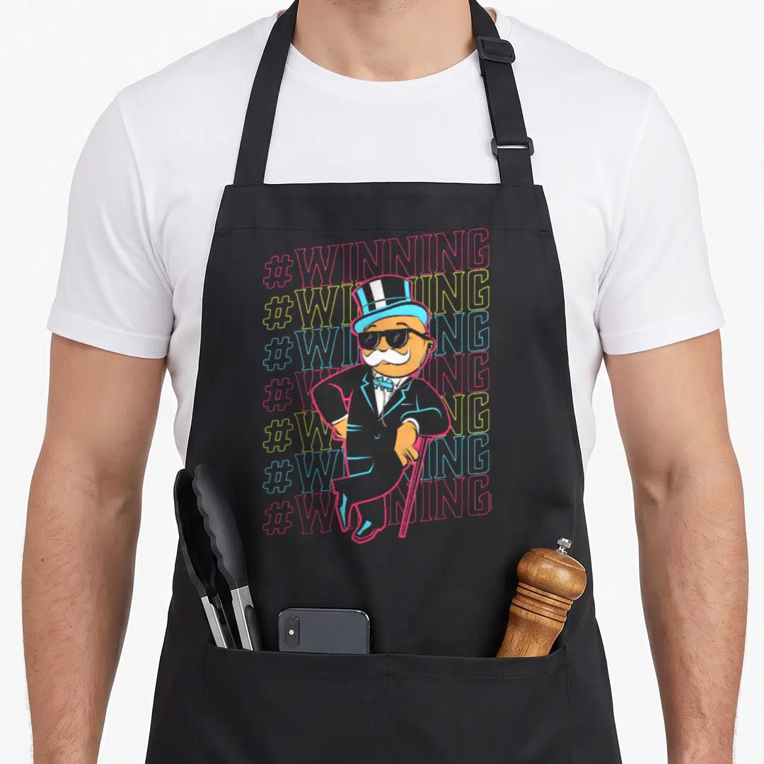 Rich monopoly apron - Cartoon man in top hat overlapping seven #WINNING hashtags in red yellow blue grey — shown on a black cotton canvas apron against a white background