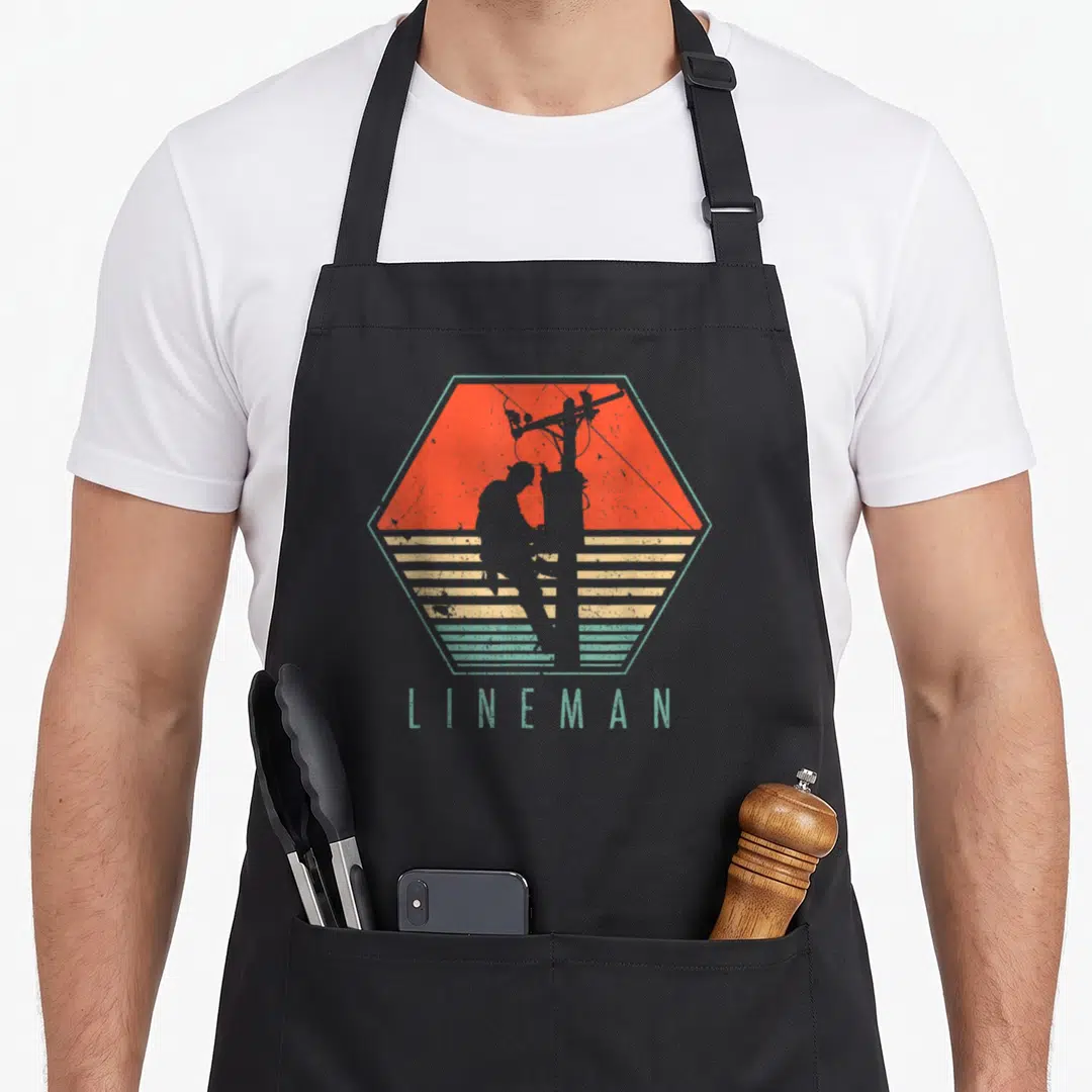 Lineman electrician apron - Retro hexagon with lineman silhouette on pole and striped background — shown on a black cotton canvas apron against a white background