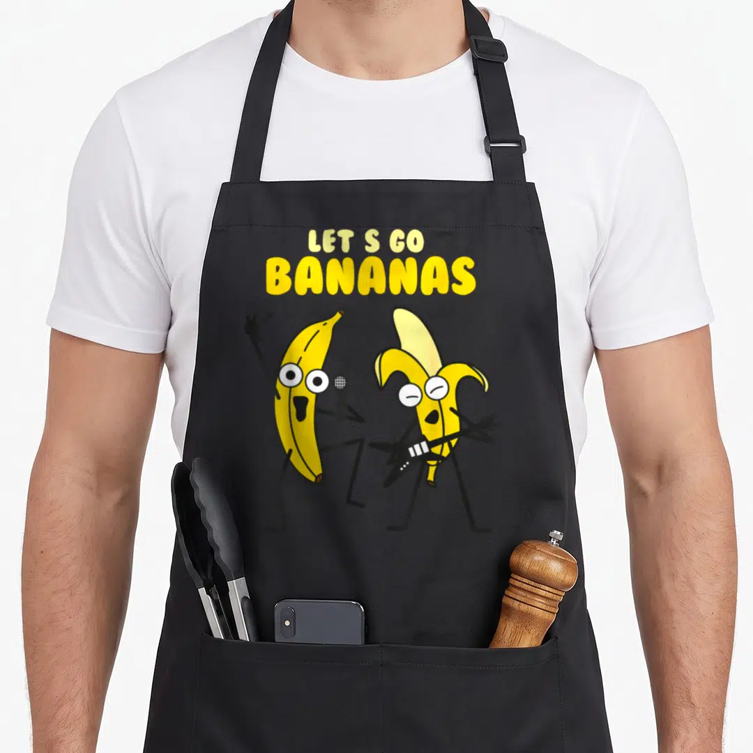 Bananas jook apron - Two cartoon bananas playing guitar and holding microphone under yellow text — shown on a black cotton canvas apron against a white background