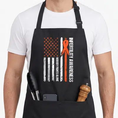 Transfer ribbon apron - Orange ribbon and distressed flag with vertical text Nobody Fights Alone — shown on a black cotton canvas apron against a white background