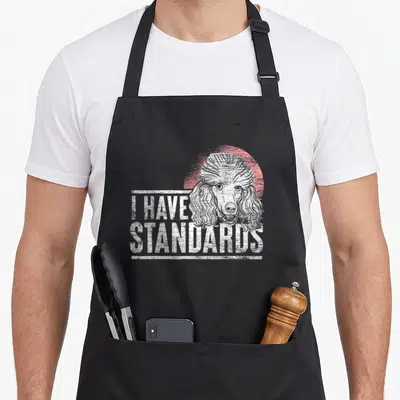 Poodle dog breed standard size of apron - White poodle head over red circle with I HAVE STANDARDS text — shown on a black cotton canvas apron against a white background