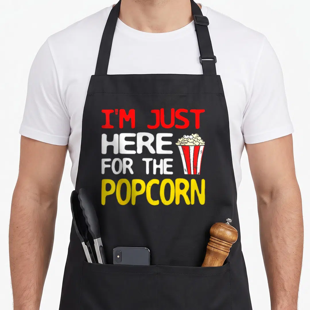 Popcorn sarcastic apron - Stacked red white and yellow text next to a red and white striped popcorn bucket — shown on a black cotton canvas apron against a white background