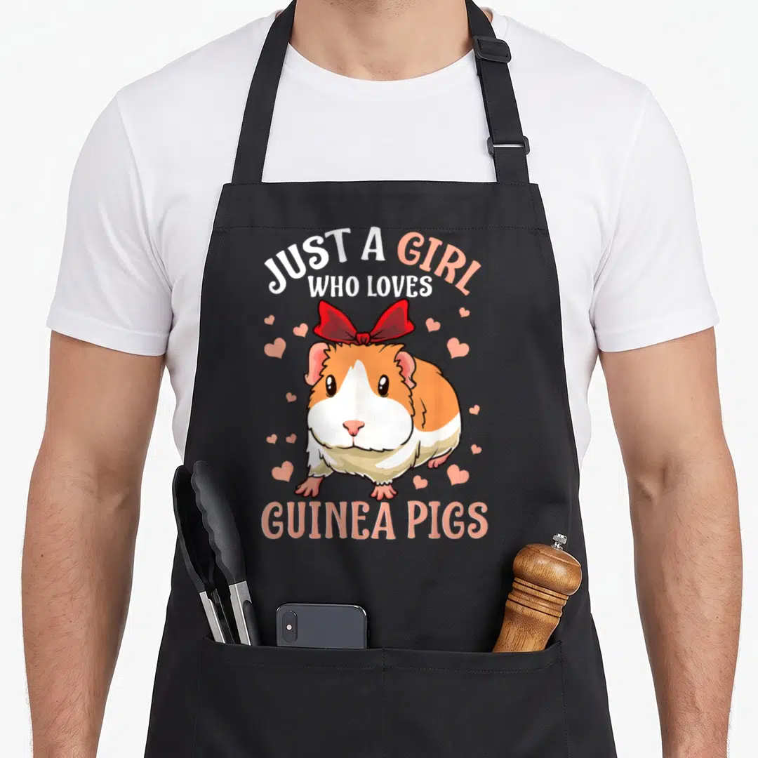 Pig cute guinea apron - Cartoon orange and white guinea pig with red bow and pink hearts under printed text — shown on a black cotton canvas apron against a white background