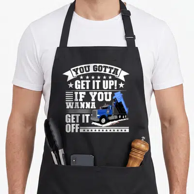 Funny dump truck apron - Blue dump truck graphic with You Gotta Get It Up text and stars — shown on a black cotton canvas apron against a white background