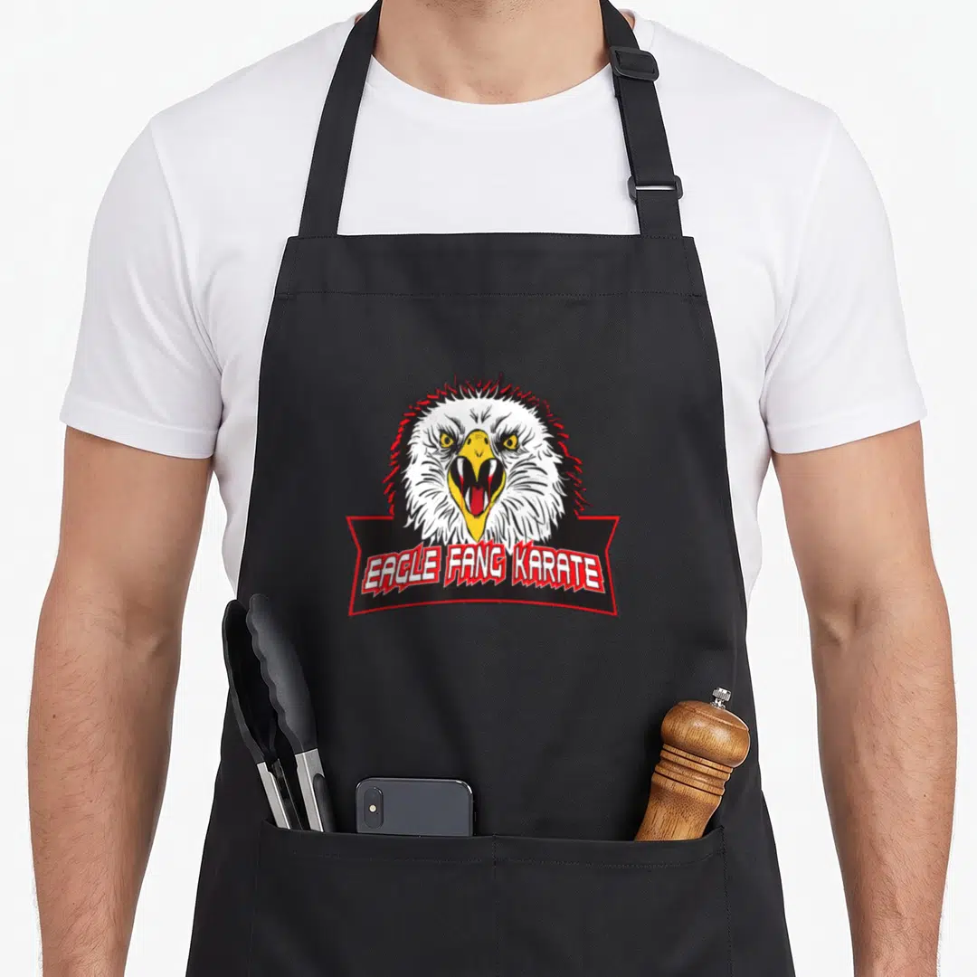 Cobra eagles apron - Eagle fang karate text below cartoon eagle head with open beak and red border — shown on a black cotton canvas apron against a white background