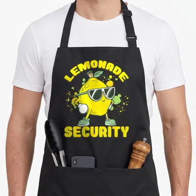 Security lemon apron - Cartoon yellow lemon in sunglasses and gloves with LEMONADE SECURITY text — shown on a black cotton canvas apron against a white background