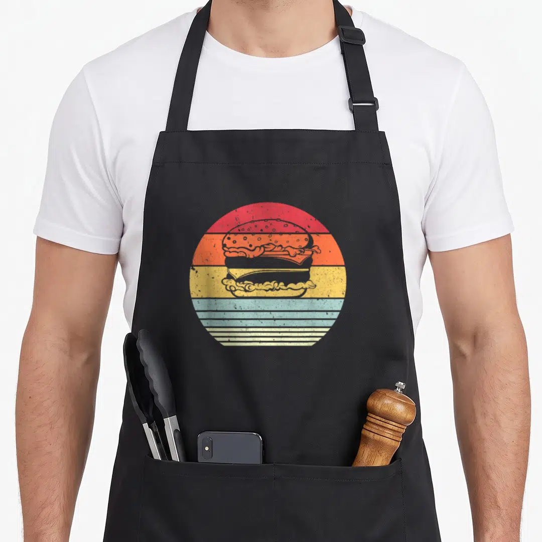 Burger hamburger casserole apron - Retro hamburger silhouette on red orange yellow teal striped circle background — shown on a black cotton canvas apron against a white background