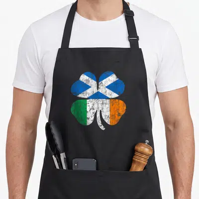 Scottish ireland apron - Distressed shamrock with Scottish saltire and Irish tricolor flag fills inside — shown on a black cotton canvas apron against a white background