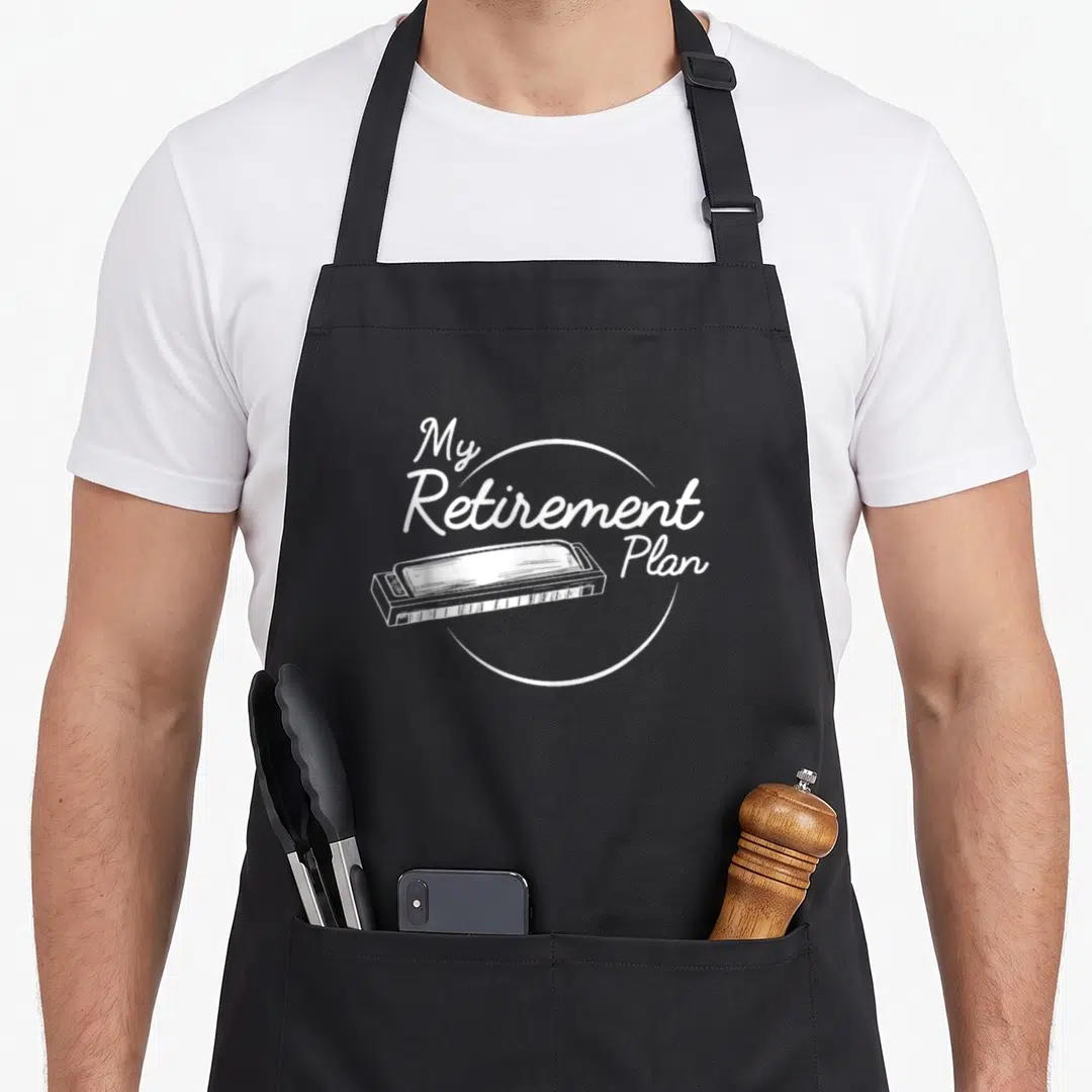 Harmonica retirement apron - White My Retirement Plan text surrounding a harmonica sketch in line art — shown on a black cotton canvas apron against a white background