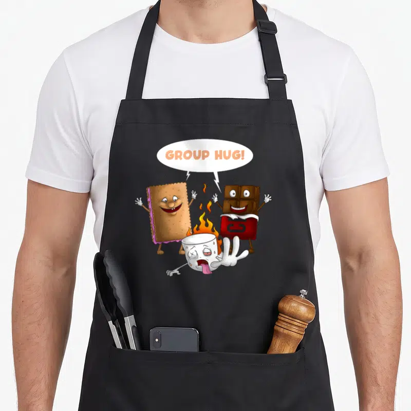 Hug food aprons - Cartoon marshmallow roasting between graham cracker and chocolate bar with GROUP HUG text — shown on a black cotton canvas apron against a white background