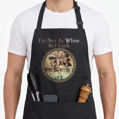Funny heritage native american aprons - Stacked text I'm Not As White As I Look above circular portrait of man — shown on a black cotton canvas apron against a white background