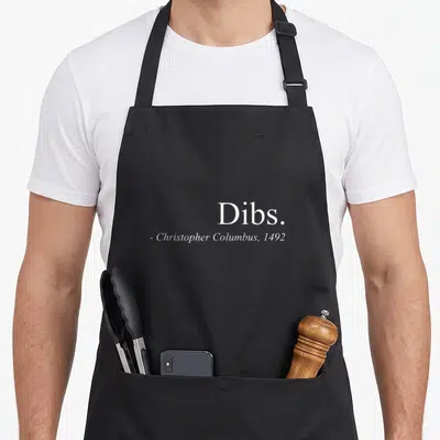 Dib columbus apron - White text Dibs Christopher Columbus 1492 typography on grey background — shown on a black cotton canvas apron against a white background