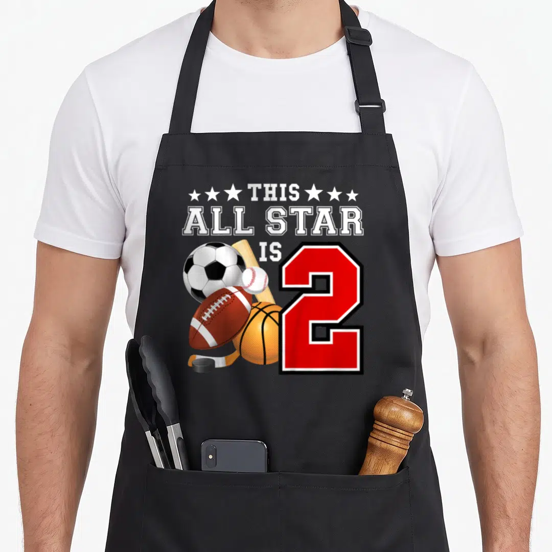 Sport 2nd apron - THIS ALL STAR IS 2 text with soccer ball, football, basketball, baseball, hockey stick and puck next — shown on a black cotton canvas apron against a white background