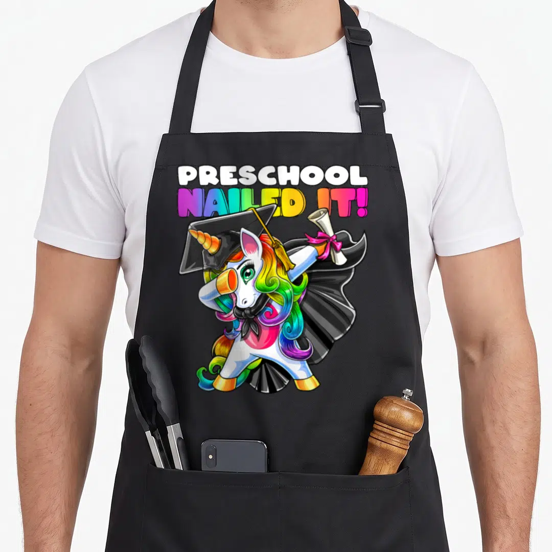 Unicorn preschool apron - Dabbing unicorn in graduation cap holding diploma under stacked text — shown on a black cotton canvas apron against a white background