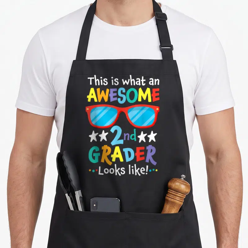 Grader 2nd apron - Colorful text This is what an AWESOME 2nd GRADER Looks like surrounding red sunglasses with blue — shown on a black cotton canvas apron against a white background