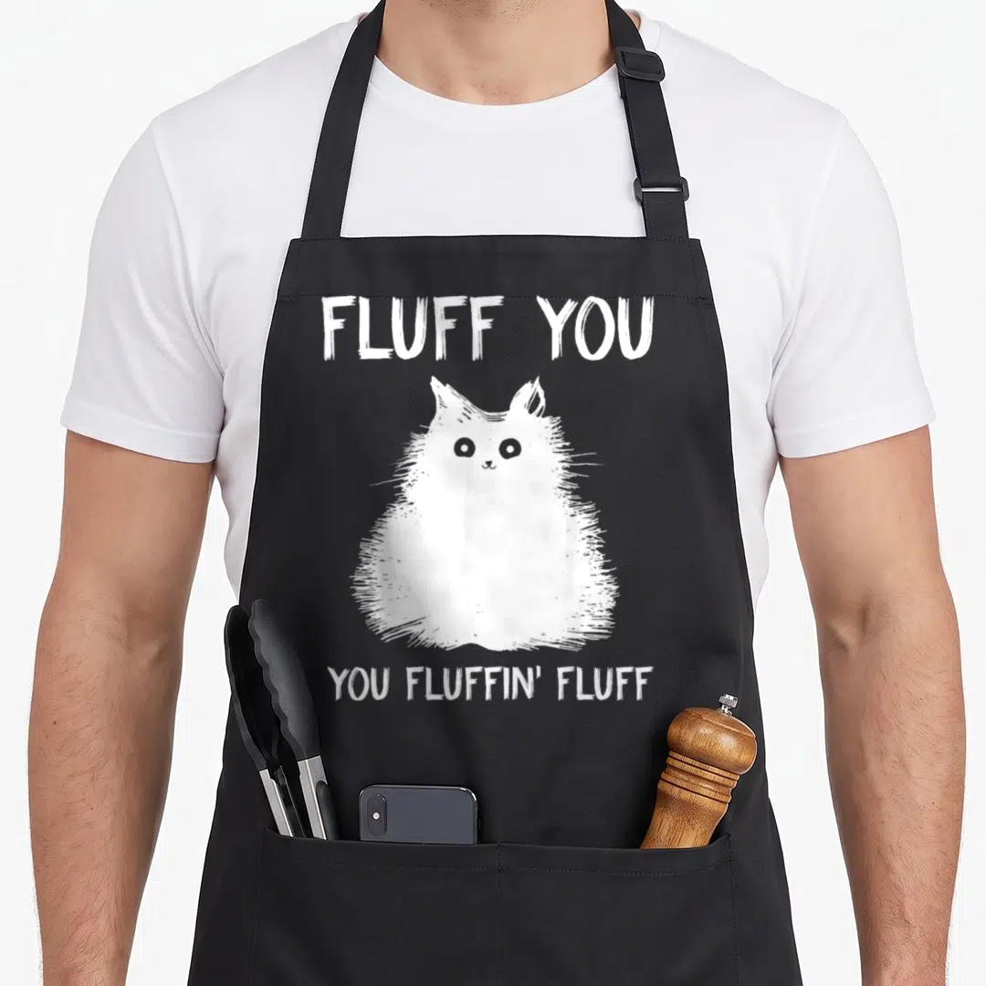 Fluff kitten apron - White cartoon cat between FLUFF YOU and YOU FLUFFIN' FLUFF text — shown on a black cotton canvas apron against a white background