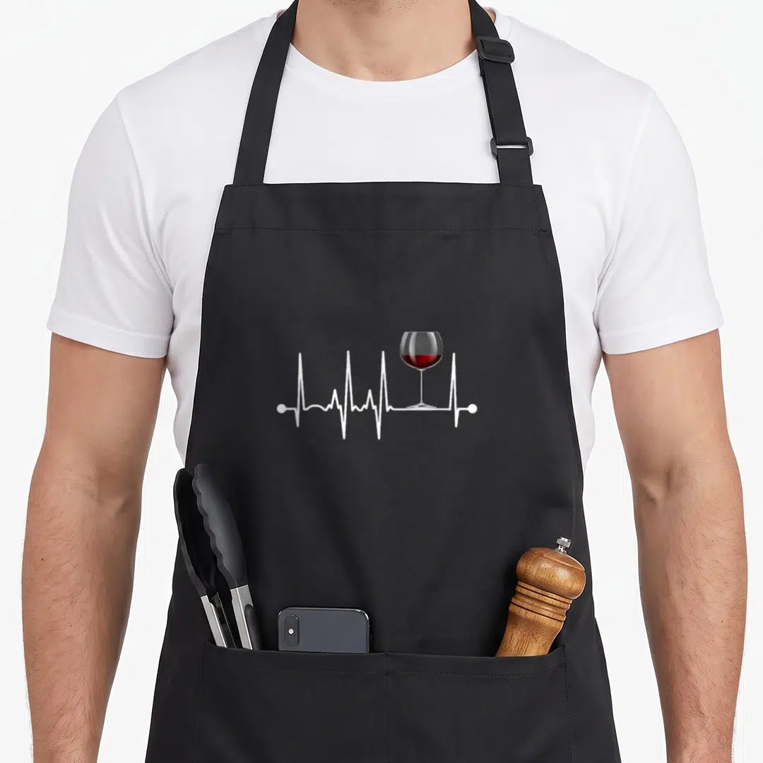 Heartbeat wine apron - White heartbeat line with red wine glass resting on the trace — shown on a black cotton canvas apron against a white background