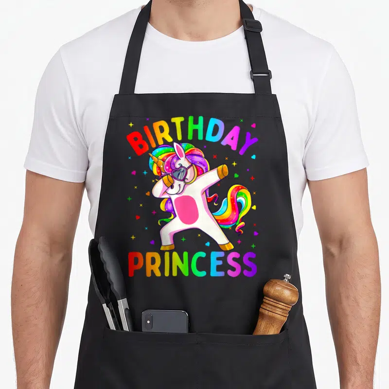 Birthday dabbing princess apron - Rainbow unicorn dabbing with sunglasses between BIRTHDAY and PRINCESS text surrounded — shown on a black cotton canvas apron against a white background