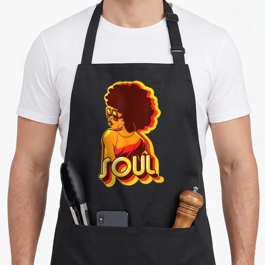 Styleuniversal 70s apron - Retro woman with afro and SOUL text in orange, yellow, and dark red — shown on a black cotton canvas apron against a white background