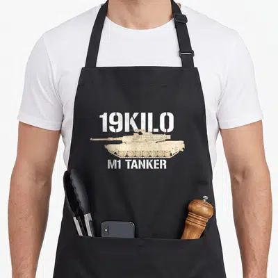 19kilo force husband apron - Distressed white 19KILO and M1 TANKER text flanking a tan Abrams tank illustration — shown on a black cotton canvas apron against a white background
