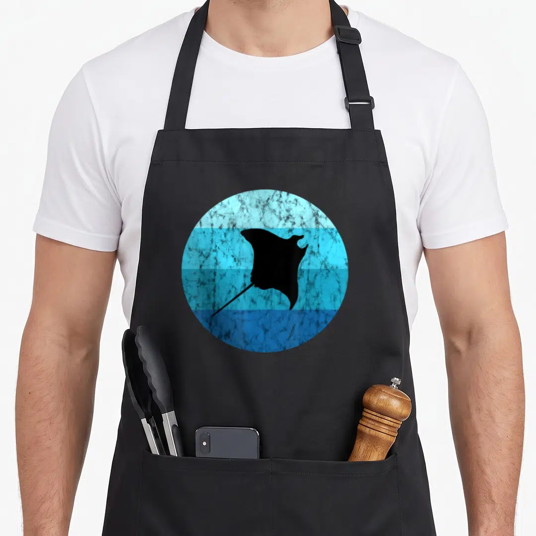 Manta biodiversity apron - Black stingray silhouette inside a textured blue circle with horizontal bands — shown on a black cotton canvas apron against a white background