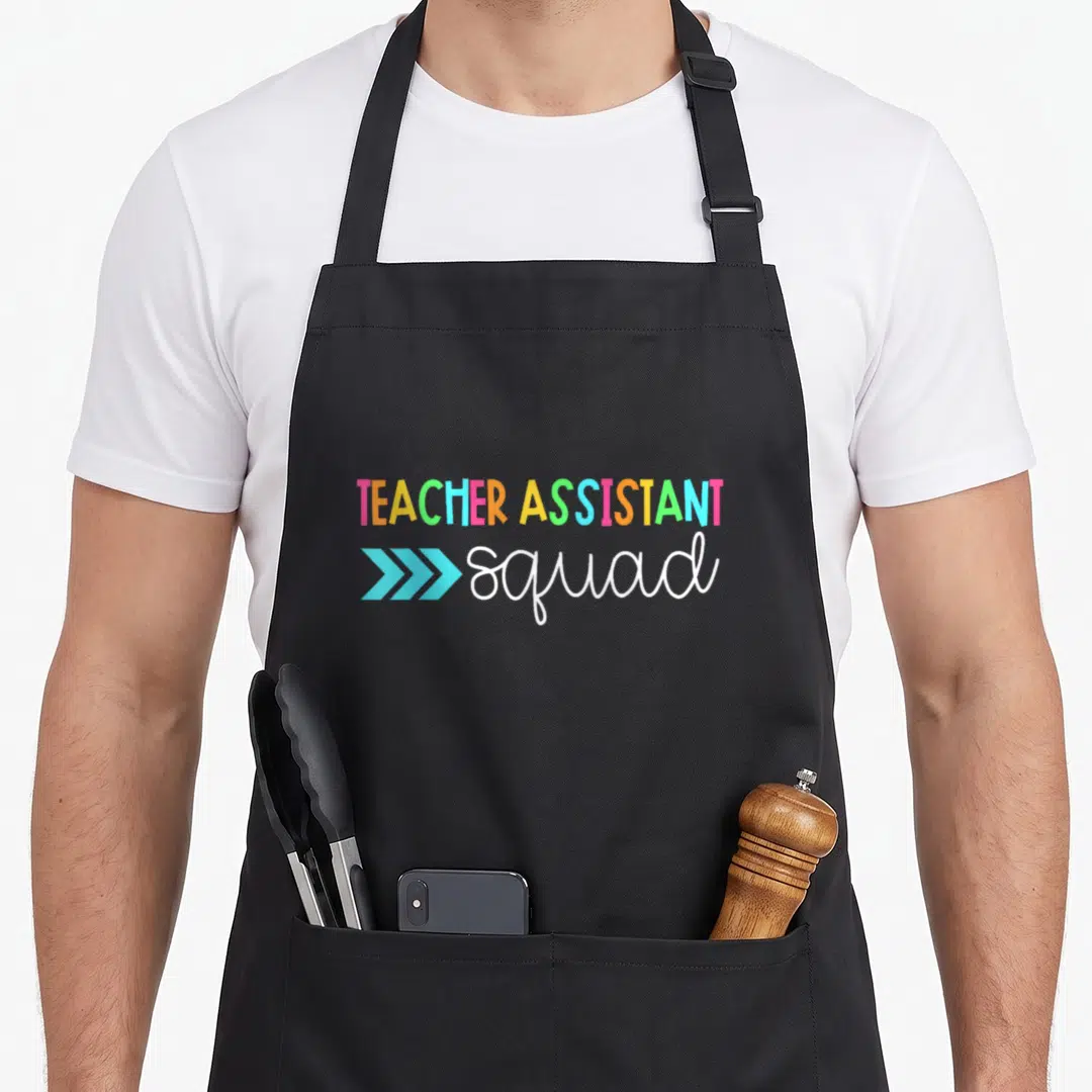 Assistant aide teacher apron - TEACHER ASSISTANT in rainbow block letters above white squad text with three blue — shown on a black cotton canvas apron against a white background