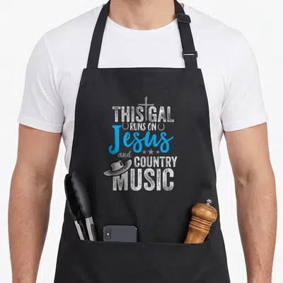 Gal country apron - Stacked text THIS GAL RUNS ON Jesus COUNTRY MUSIC with grey cross blue script and cowboy hat — shown on a black cotton canvas apron against a white background
