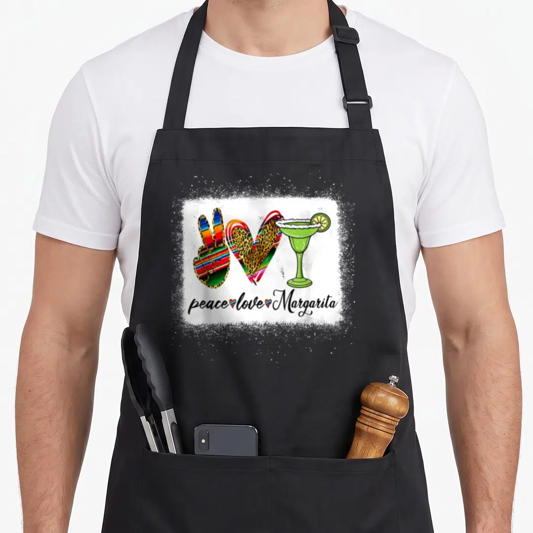 Peace margarita apron - Peace sign, leopard heart, and green margarita glass above script text on white splatter — shown on a black cotton canvas apron against a white background