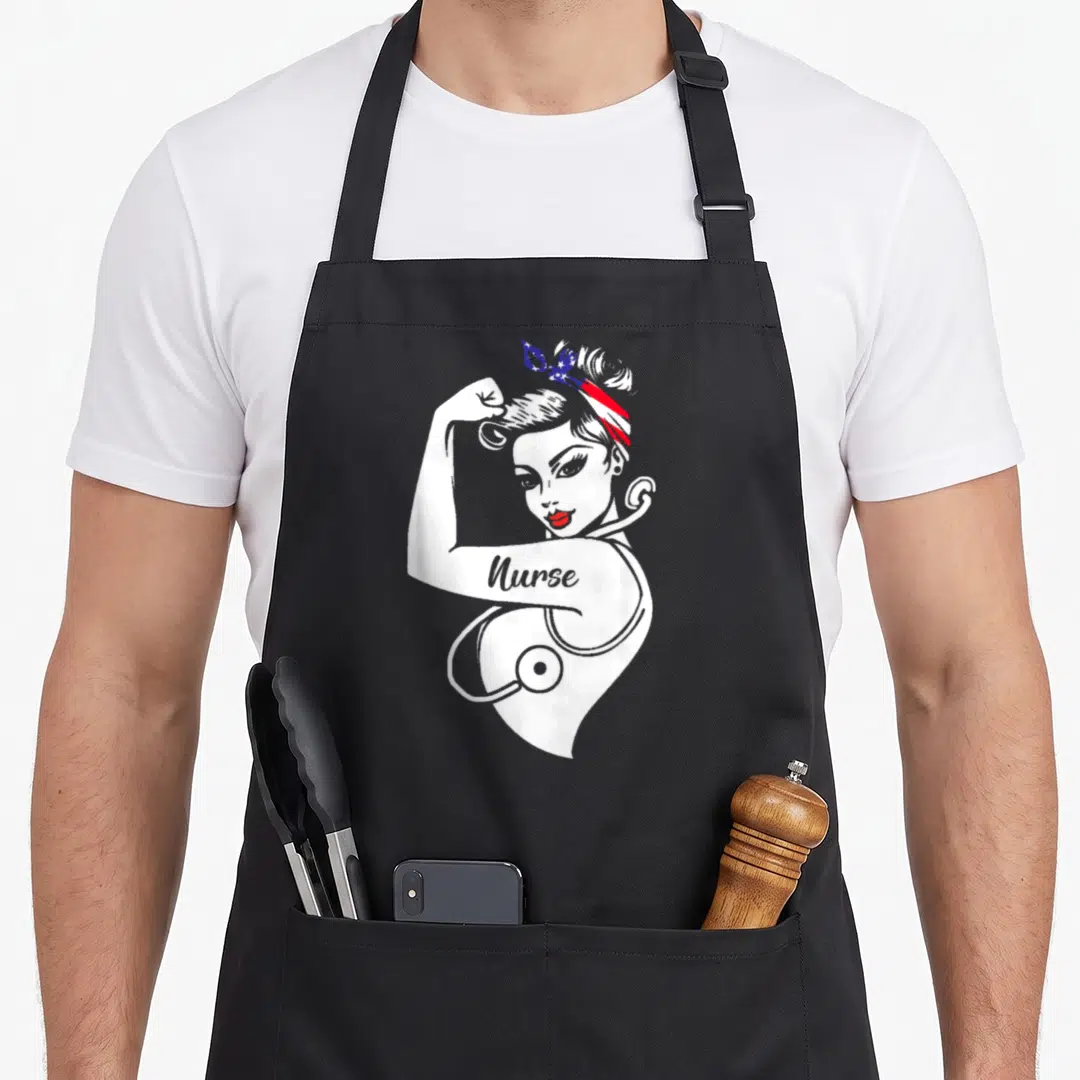Nurse american flag apron - Cartoon strong woman flexing arm with Nurse text and stethoscope wearing patriotic headscarf — shown on a black cotton canvas apron against a white background
