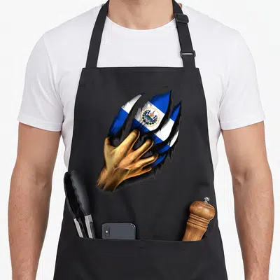 Cute salvador salvadoran apron - Gold hand tearing through surface revealing Salvadoran flag and national text — shown on a black cotton canvas apron against a white background