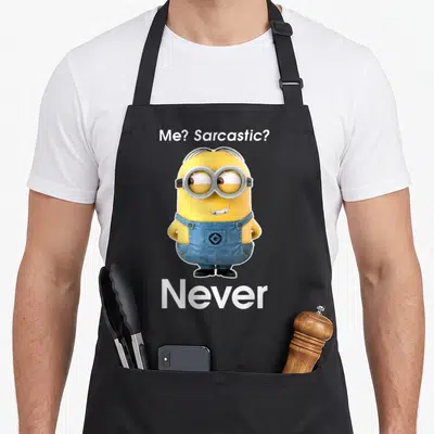 Despicable sarcastic apron - Yellow minion centered between white text Me Sarcastic Never Never on black background — shown on a black cotton canvas apron against a white background