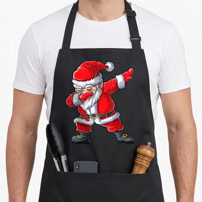 Dabbing santa claus apron - Cartoon Santa Claus character in a dab pose wearing a red suit with white fur trim — shown on a black cotton canvas apron against a white background
