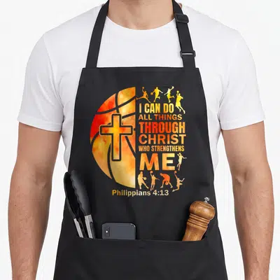 Basketball christian apron - Cross inside basketball with player silhouettes and Philippians 4:13 text in orange and red — shown on a black cotton canvas apron against a white background