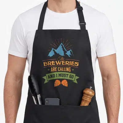 Drinking brewery craft apron - Blue mountains and orange rays above stacked text inside a green banner with two orange — shown on a black cotton canvas apron against a white background