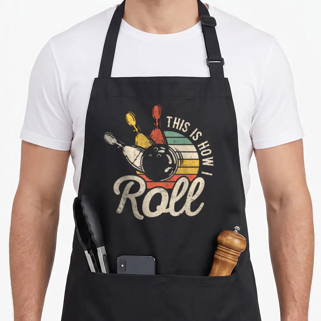 Bowling roll apron - Retro bowling ball and pins over striped sun with off-white text — shown on a black cotton canvas apron against a white background