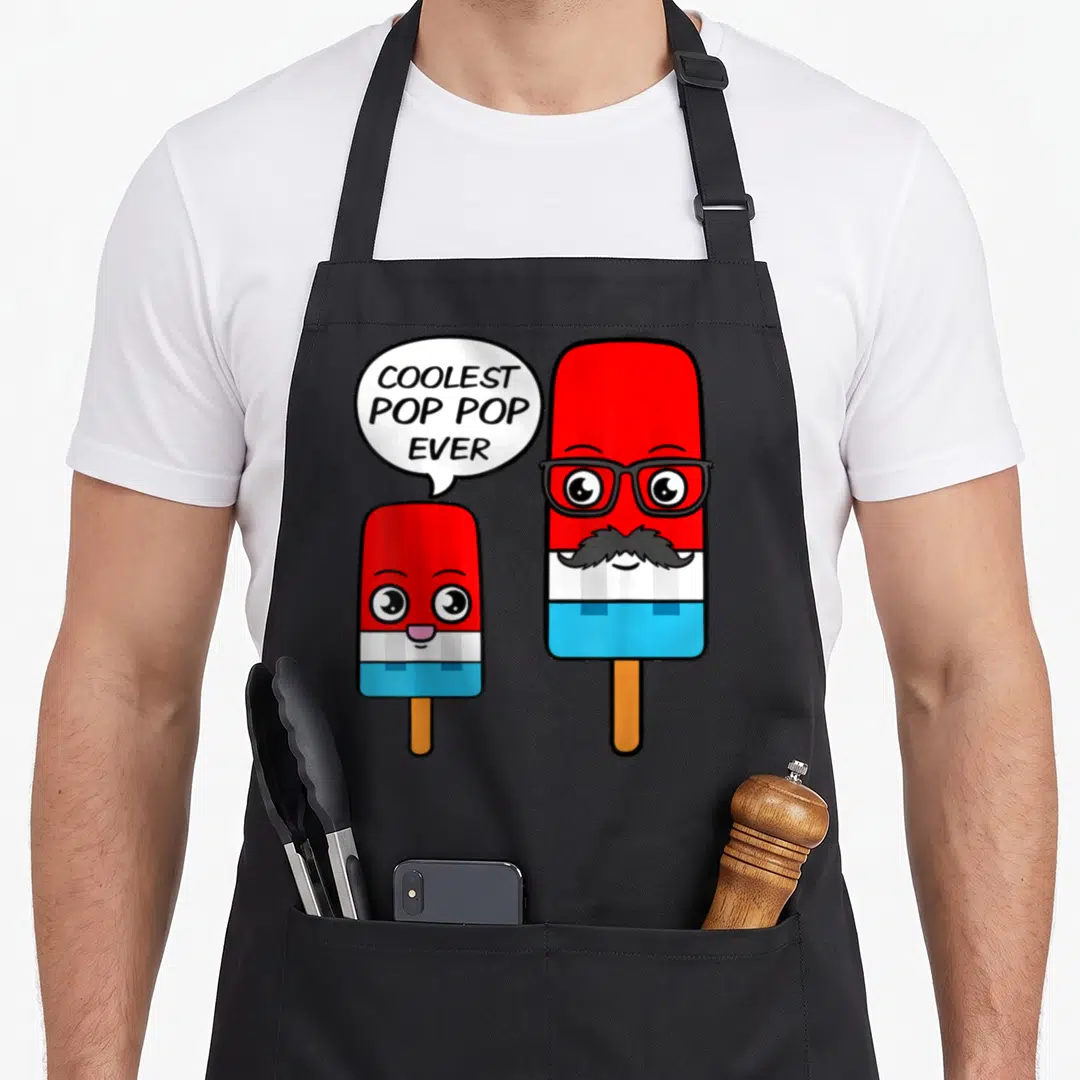 Coolest ice cream apron - Two red white and blue popsicles, one with glasses and mustache, speech bubble says COOLEST — shown on a black cotton canvas apron against a white background
