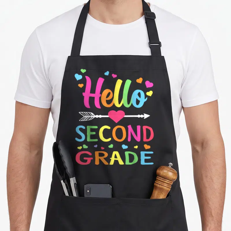 School teacher 2nd apron - Hello Second Grade text with arrow through heart and scattered colorful hearts — shown on a black cotton canvas apron against a white background