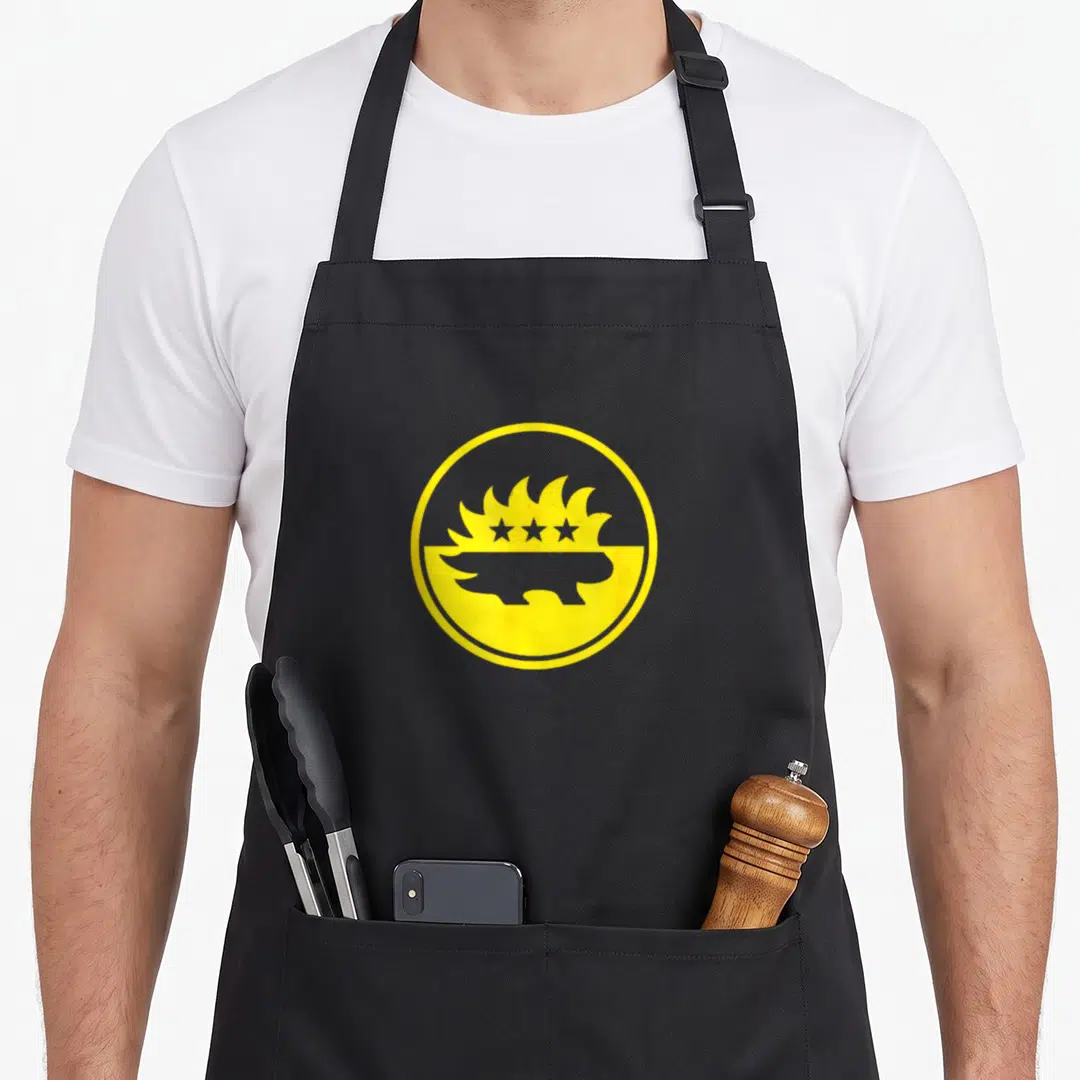 Libertarian porcupine apron - Yellow circle logo with porcupine silhouette, four stars, and flames — shown on a black cotton canvas apron against a white background