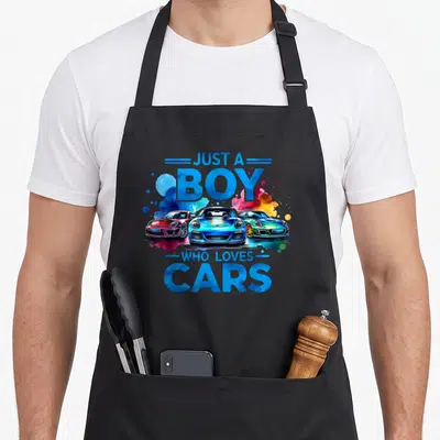Sleek car apron - Three colorful sports cars with watercolor splashes and blue text JUST A BOY WHO LOVES CARS — shown on a black cotton canvas apron against a white background