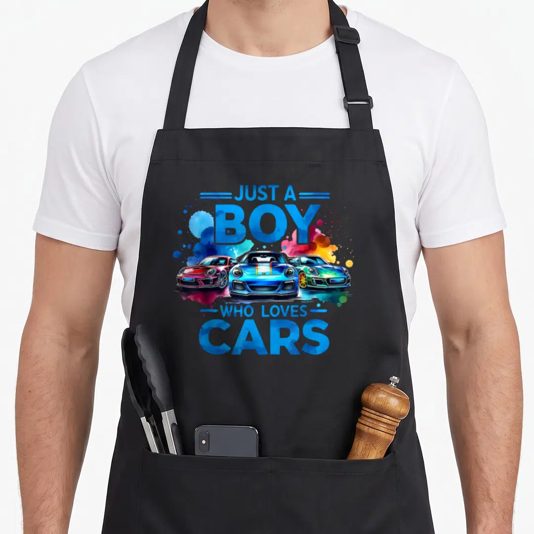 Sleek car apron - Three colorful sports cars with watercolor splashes and blue text JUST A BOY WHO LOVES CARS — shown on a black cotton canvas apron against a white background