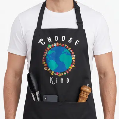 Choose teacher apron - CHOOSE KIND text around blue green earth with diverse cartoon figures on black fabric — shown on a black cotton canvas apron against a white background