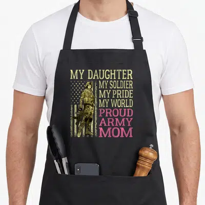 Soldier mother daughter apron - Female soldier standing before yellow stars and pink text reading My Daughter My — shown on a black cotton canvas apron against a white background