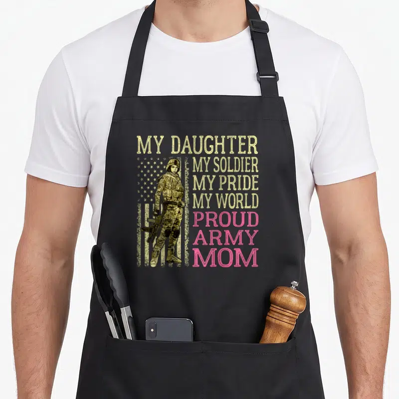 Soldier mother daughter apron - Female soldier standing before yellow stars and pink text reading My Daughter My — shown on a black cotton canvas apron against a white background